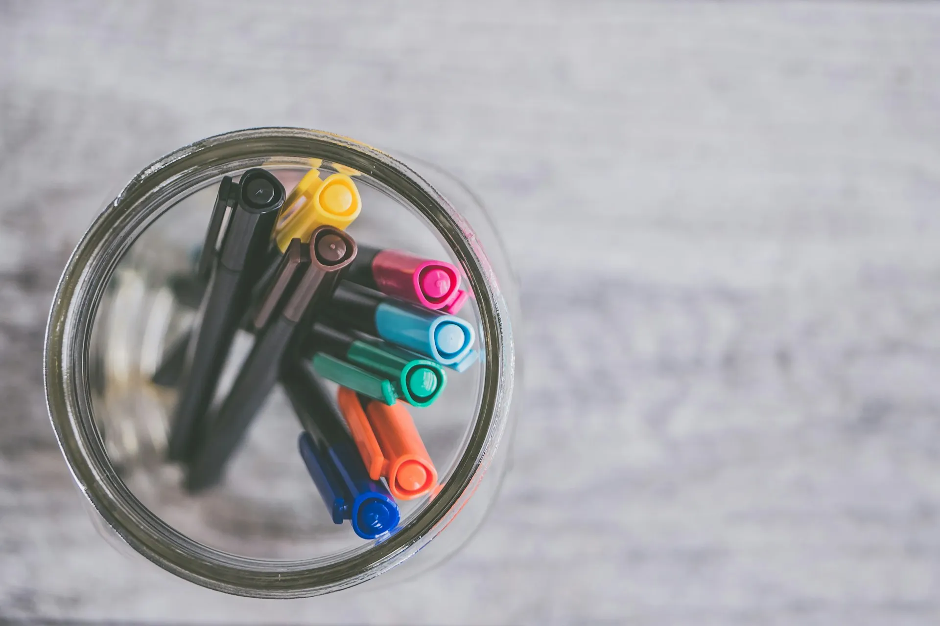 Colorful markers and pens arranged in a jar on a wooden desk